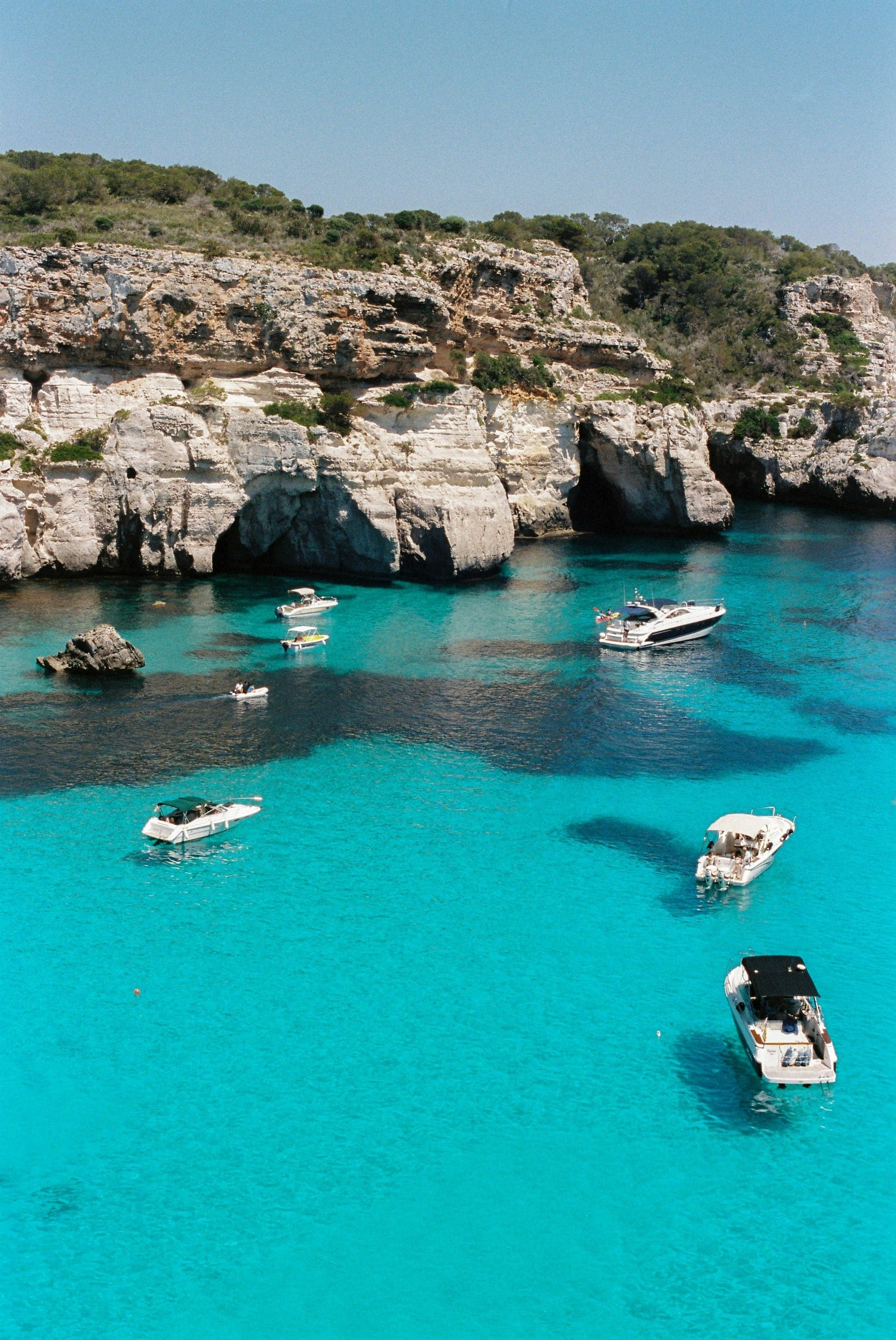 Small boats in a bright turquoise cala under limestone cliffs