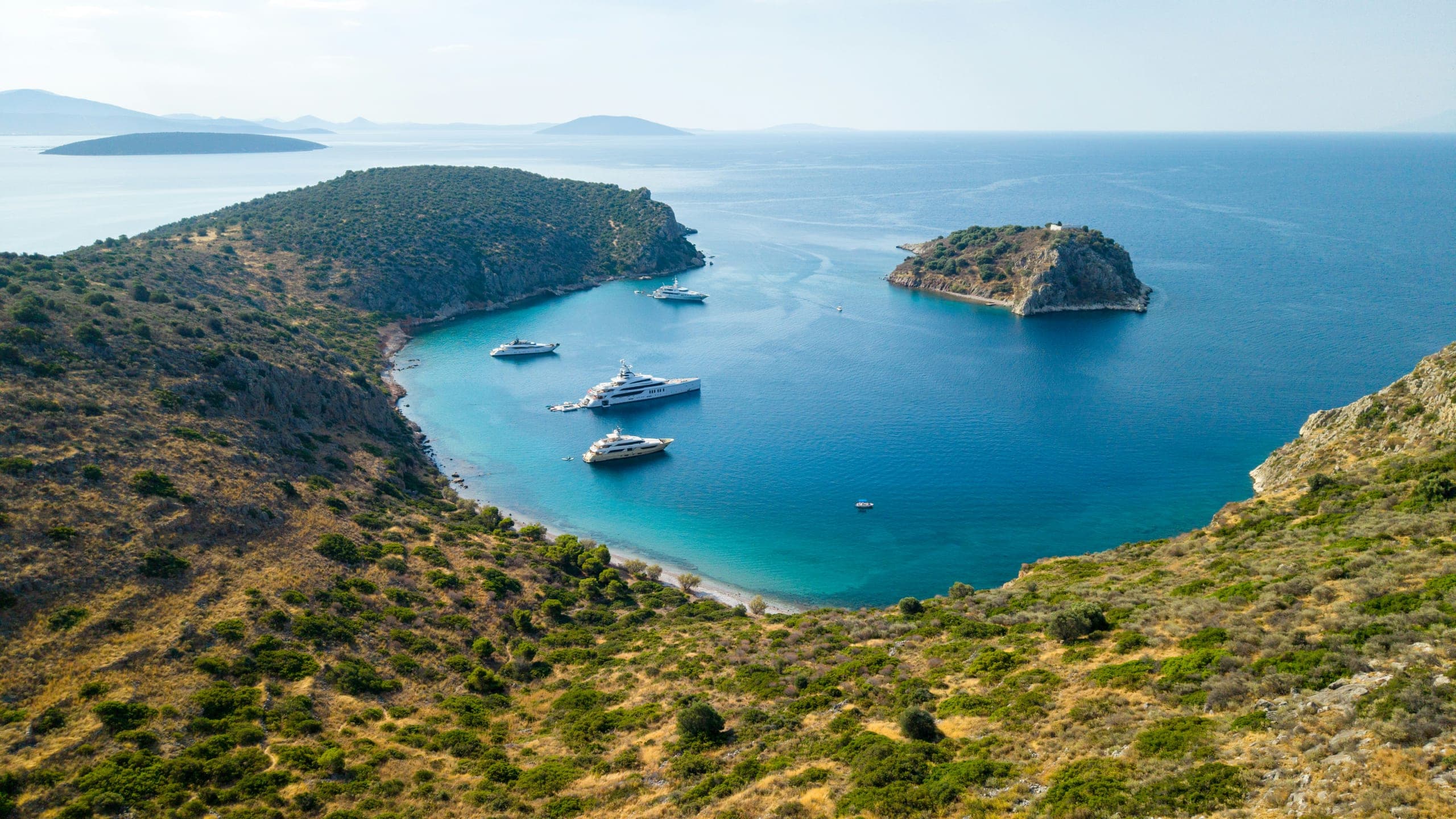 A sheltered bay on the Aegean, three yachts at anchor below a scrub-covered headland